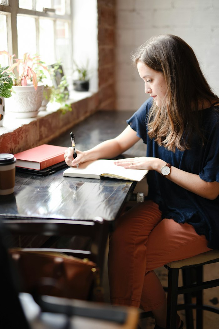 A woman writing in a notebook by a sunny window