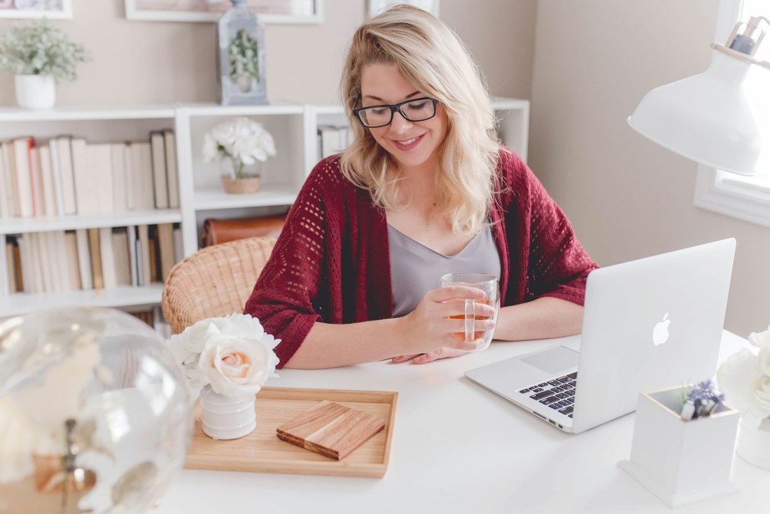 A smiling woman with a mug of tea working on her laptop at home