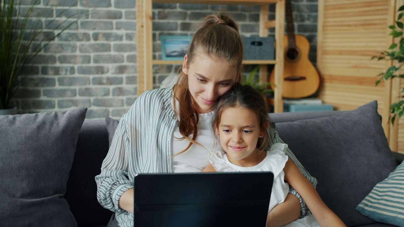 A mother and her daughter smiling at a laptop together on the couch