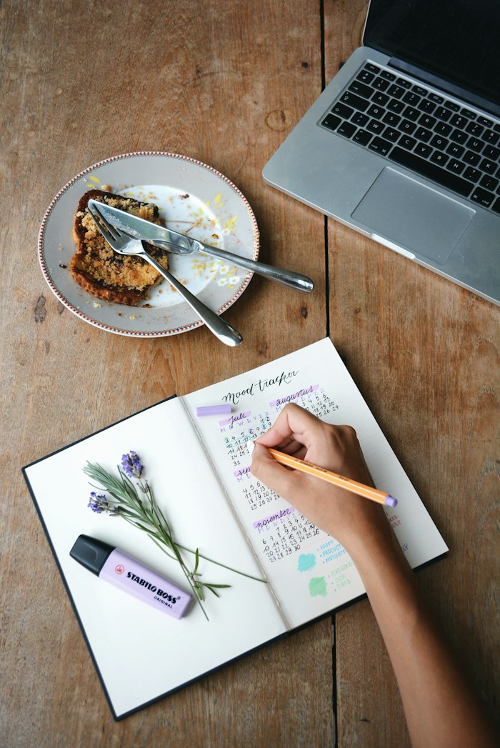 A hand writing in a planner next to a laptop