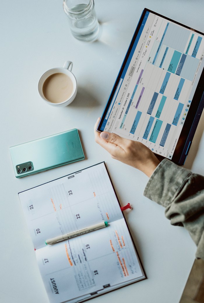 A tablet with a calendar beside a coffee and planner